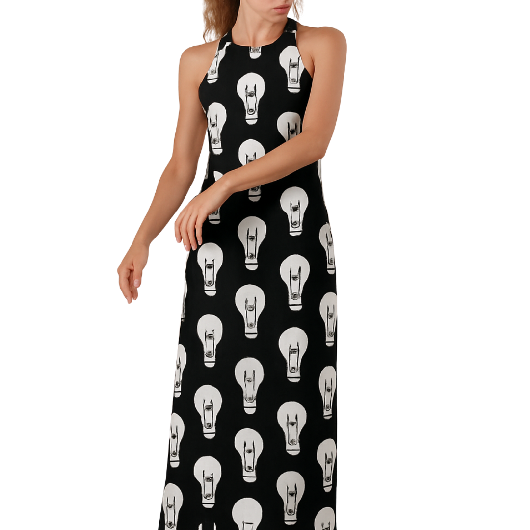 Woman wearing a black halter maxi dress with white lightbulb print, titled Maxi-Mum Voltage, standing barefoot.