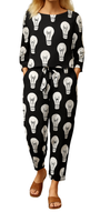 Woman wearing Lit Up Co-ord Set with black fabric covered in white hand-drawn light bulb motifs, paired with brown sandals.