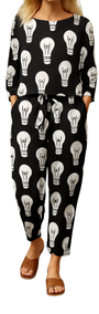 Woman wearing Lit Up Co-ord Set with black fabric covered in white hand-drawn light bulb motifs, paired with brown sandals.