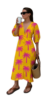 Woman wearing Tropic Like It’s Hot dress with flamingo-pink palms on sunshine-yellow, carrying a woven bag and holding a coffee cup.