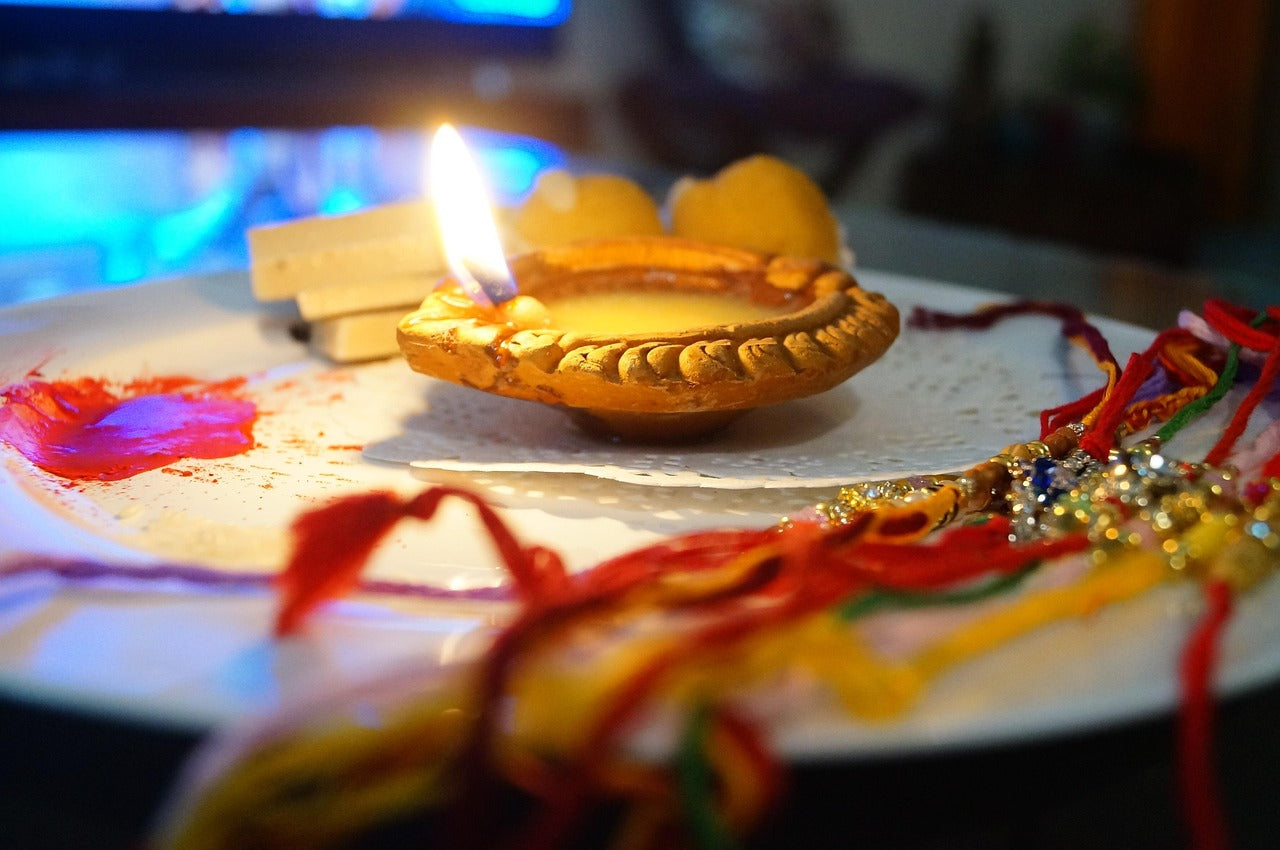Rakhi Gift Card featuring a traditional diya lamp, vibrant rakhis, and festive decorations on a plate.